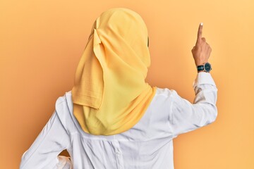 Young brunette arab woman wearing traditional islamic hijab scarf posing backwards pointing ahead...