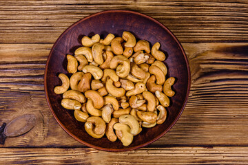Ceramic plate with roasted cashew nuts on a wooden table. Top view