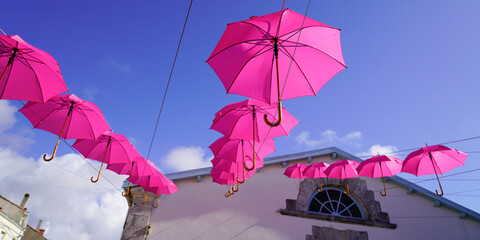 pink umbrellas hang between houses street decorated