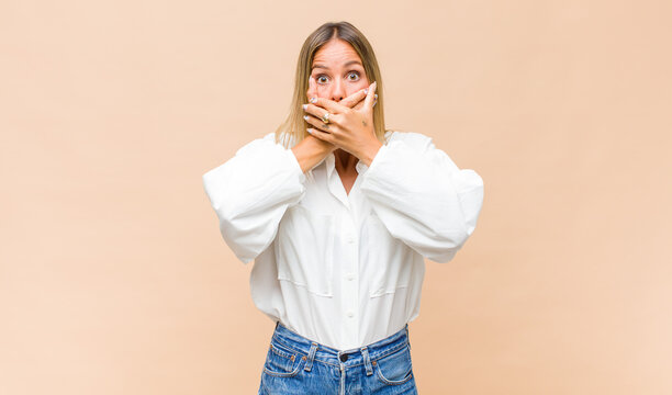 young pretty woman covering mouth with hands with a shocked, surprised expression, keeping a secret or saying oops