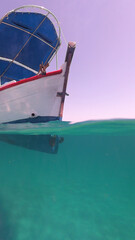 Underwater split photo of traditional wooden fishing boat in Aegean island, with emerald clear sea, Greece