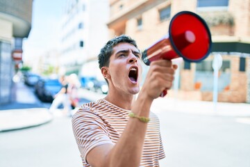 Young handsome caucasian man screaming using megaphone at city