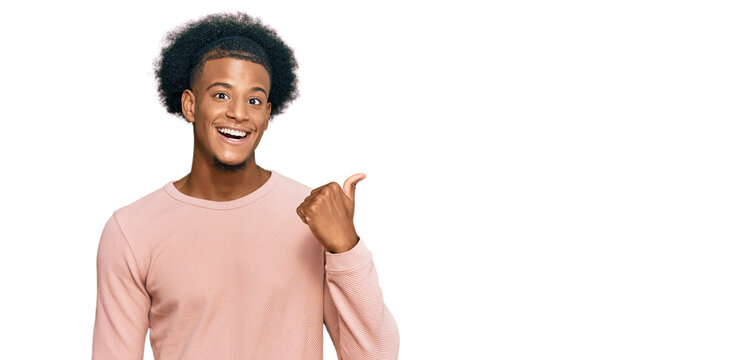 African american man with afro hair wearing casual clothes smiling with happy face looking and pointing to the side with thumb up.