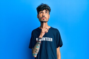 Young hispanic man wearing volunteer t shirt thinking concentrated about doubt with finger on chin...