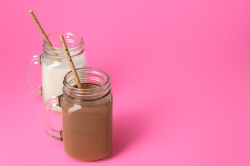 Glass jars with flavoured milkshakes against pink background