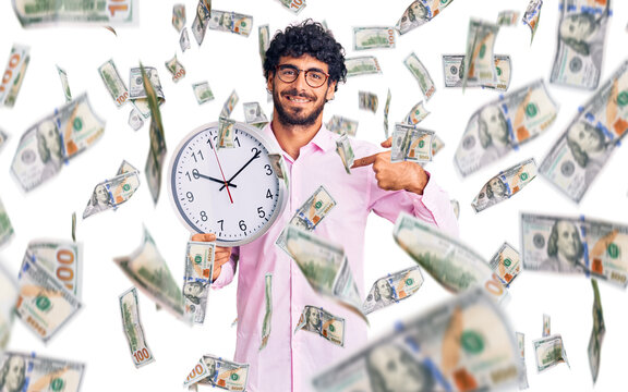 Handsome young man with curly hair and bear holding big clock pointing finger to one self smiling happy and proud