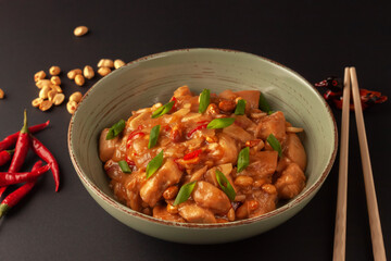 Kung Bao chicken on a black background. A Chinese dish with chicken, chili, peanuts, sauces and onions.