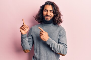 Young arab man wearing casual clothes smiling and looking at the camera pointing with two hands and fingers to the side.