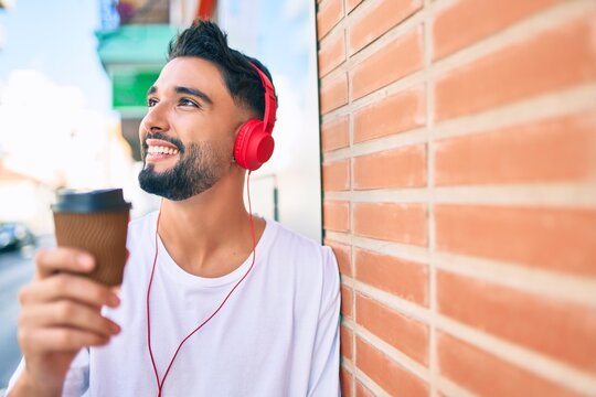 Young arab man drinking take away coffee and using headphones at the city.