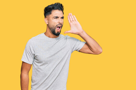 Young man with beard wearing casual grey tshirt shouting and screaming loud to side with hand on mouth. communication concept.