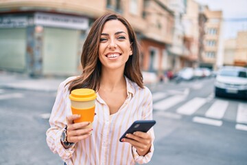 Young hispanic woman smiling happy using smartphone and drinking take away coffee at the city.