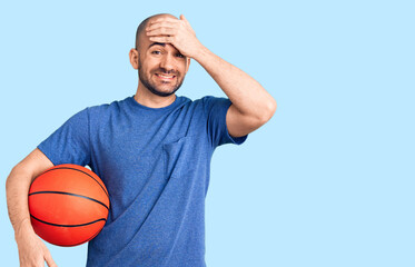 Young handsome man holding basketball ball stressed and frustrated with hand on head, surprised and angry face