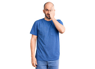 Young handsome man wearing casual t shirt covering one eye with hand, confident smile on face and surprise emotion.