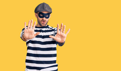 Young handsome man wearing burglar mask doing stop gesture with hands palms, angry and frustration...