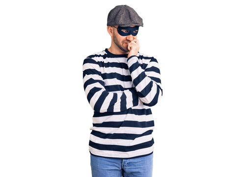 Young handsome man wearing burglar mask looking stressed and nervous with hands on mouth biting nails. anxiety problem.