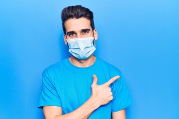 Young handsome man with beard wearing medical mask smiling cheerful pointing with hand and finger...