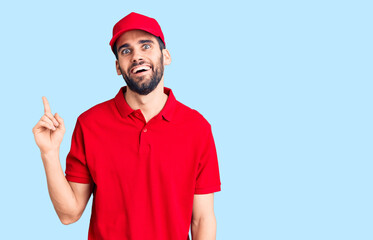 Young handsome man with beard wearing delivery uniform with a big smile on face, pointing with hand finger to the side looking at the camera.