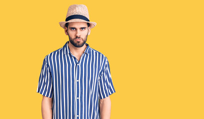 Young handsome man with beard wearing summer hat and striped shirt skeptic and nervous, frowning...