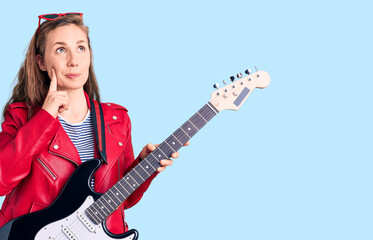 Fototapeta premium Young beautiful blonde woman playing electric guitar serious face thinking about question with hand on chin, thoughtful about confusing idea