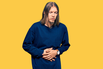 Handsome caucasian man with long hair wearing casual winter sweater with hand on stomach because indigestion, painful illness feeling unwell. ache concept.