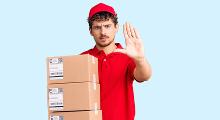 Young handsome man with curly hair holding delivery package with open hand doing stop sign with serious and confident expression, defense gesture