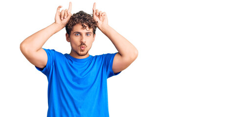 Young handsome man with curly hair wearing casual clothes doing funny gesture with finger over head as bull horns