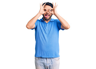 Fototapeta premium Young hispanic man wearing casual clothes doing ok gesture like binoculars sticking tongue out, eyes looking through fingers. crazy expression.