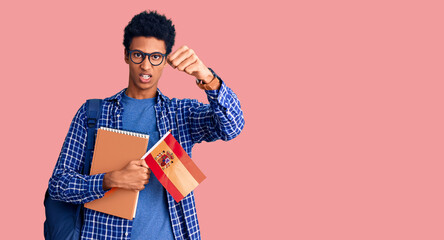 Young african american man wearing student backpack holding spanish flag annoyed and frustrated shouting with anger, yelling crazy with anger and hand raised