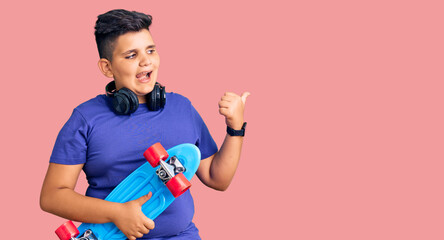 Little boy kid holding skate and wearing headphones pointing thumb up to the side smiling happy with open mouth © Krakenimages.com