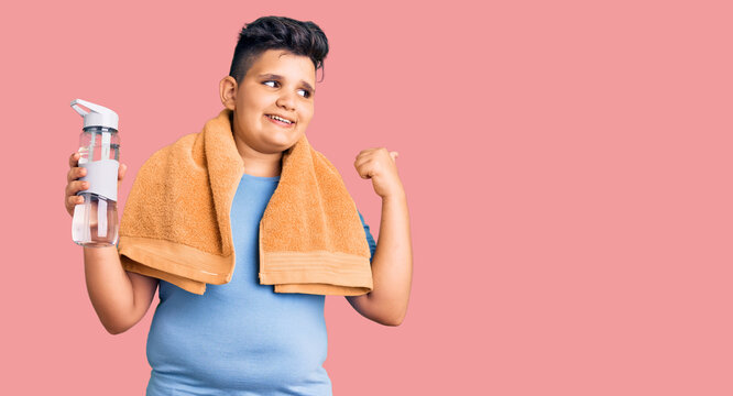 Little boy kid wearing sportswear drinking bottle of water pointing thumb up to the side smiling happy with open mouth