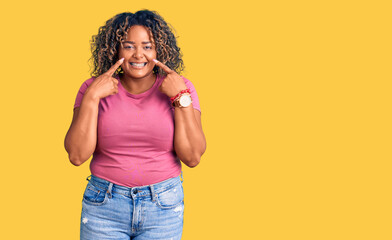 Young african american plus size woman wearing casual clothes smiling with open mouth, fingers pointing and forcing cheerful smile