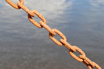 Close Up of Old Rusty Metal Chain with Water in Background 