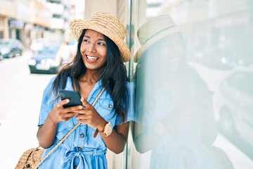 Young indian woman leaning on the wall using smartphone at the city