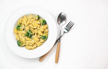 Pasta with green vegetables, broccoli, melted cheese and creamy sauce in white bowl on white table.