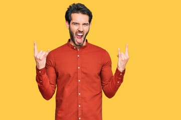 Young hispanic man wearing casual clothes shouting with crazy expression doing rock symbol with hands up. music star. heavy concept.