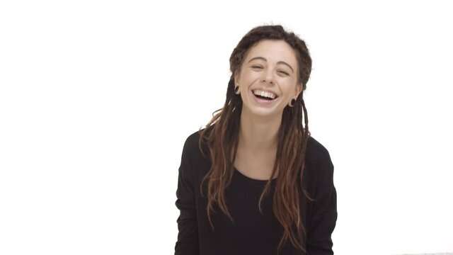 Attractive caucasian woman with dreadlocks and ear tunnels, starting to laugh from something funny, chuckling over joke, standing against white background