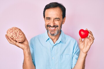 Middle age hispanic man holding brain and heart winking looking at the camera with sexy expression,...