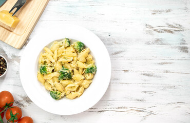 Pasta with green vegetables, broccoli, melted cheese and creamy sauce in white bowl on white table.