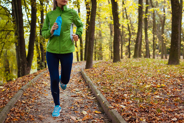 Runner working out in autumn park. Young woman running with water bottle. Active healthy lifestyle