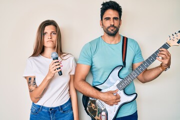 Beautiful young couple of boyfriend and girlfriend singing song using microphone and guitar relaxed with serious expression on face. simple and natural looking at the camera.