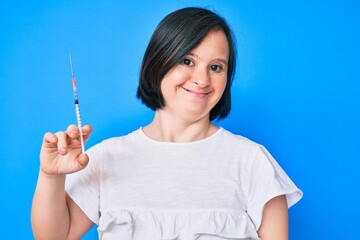 Brunette woman with down syndrome holding syringe looking positive and happy standing and smiling with a confident smile showing teeth