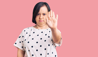 Brunette woman with down syndrome wearing casual clothes doing stop sing with palm of the hand....