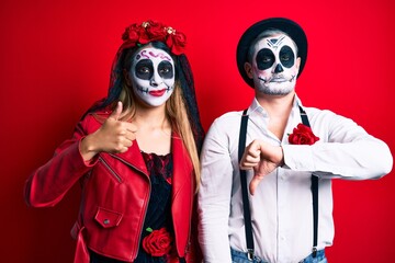 Fototapeta na wymiar Couple wearing day of the dead costume over red doing thumbs up and down, disagreement and agreement expression. crazy conflict