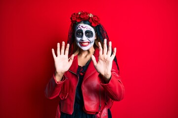 Woman wearing day of the dead costume over red afraid and terrified with fear expression stop gesture with hands, shouting in shock. panic concept.