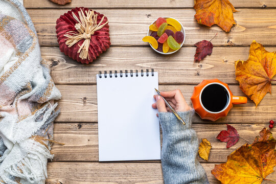 Desktop mock up planner. Top view composition with woman's hands in sweater, pumpkin styled cup of coffee and autumn themed decoration, fallen leaves on wooden background. Flat lay, copy space.