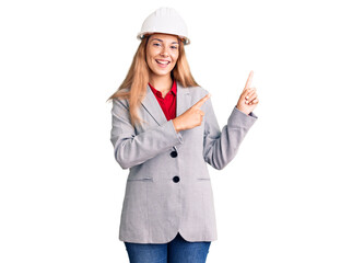 Beautiful young woman wearing architect hardhat smiling and looking at the camera pointing with two hands and fingers to the side.