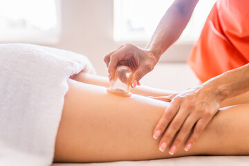Obraz na płótnie Canvas Masseur make massage with jars of cellulite on the buttock and thighs of patient. Treatment of excess weight, anti-cellulite, skin care