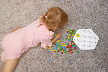 Naklejka premium Board games that develop fine motor skills. The kid girl collects a constructor puzzle from multi-colored plastic parts, top view