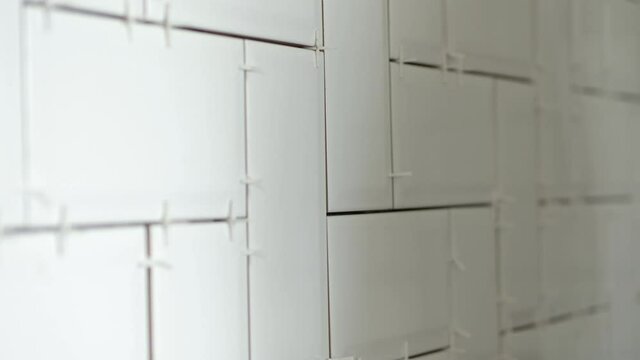 Working tiler laying white ceramic tile in a herringbone pattern on wall in kitchen.