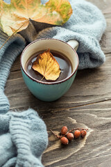 Autumn morning coffee. A cup of coffee on a wooden table and a warm sweater on a background of autumn leaves. Still life concept.